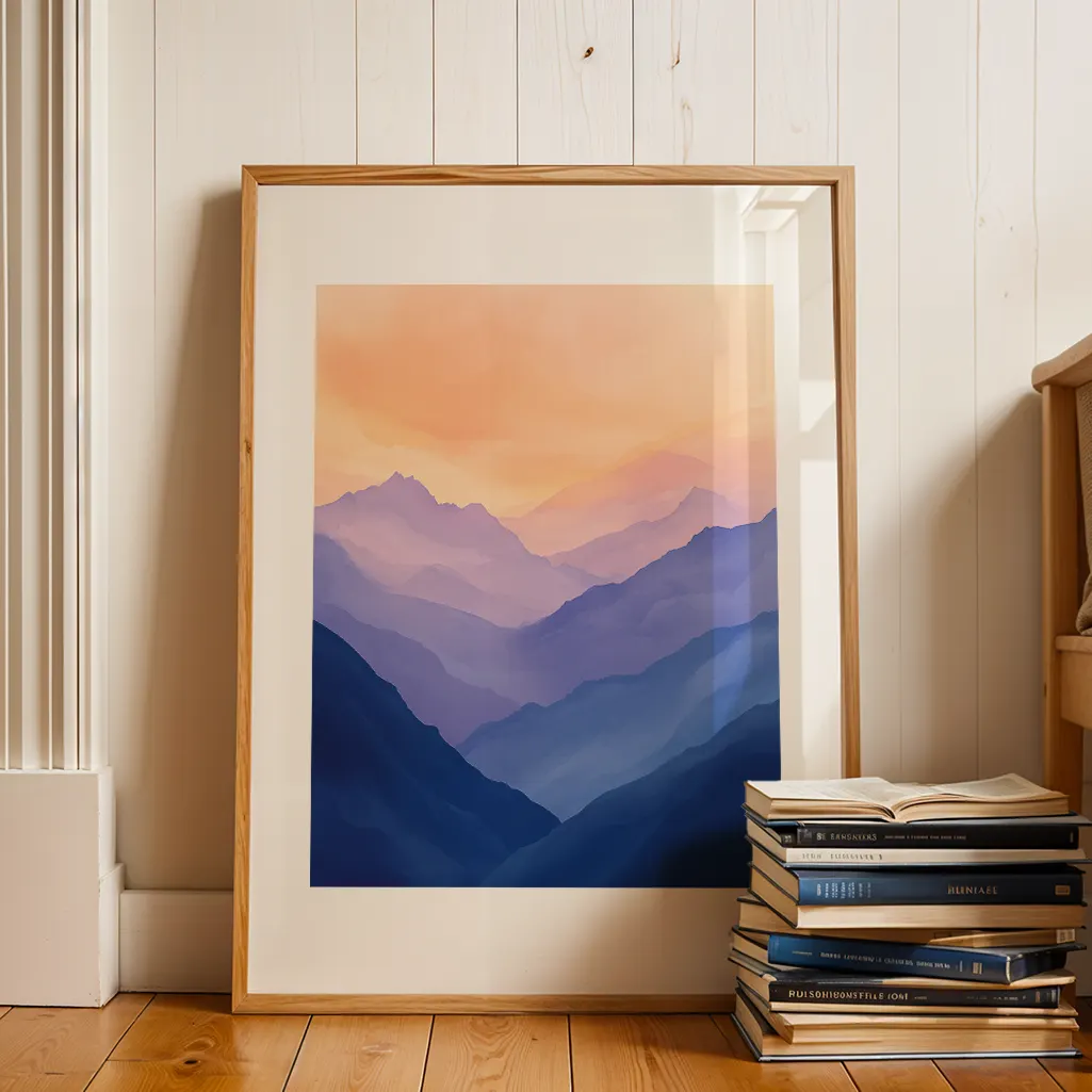 Framed mountain landscape print leaning against a white wooden wall, next to a stack of books on a wooden floor.