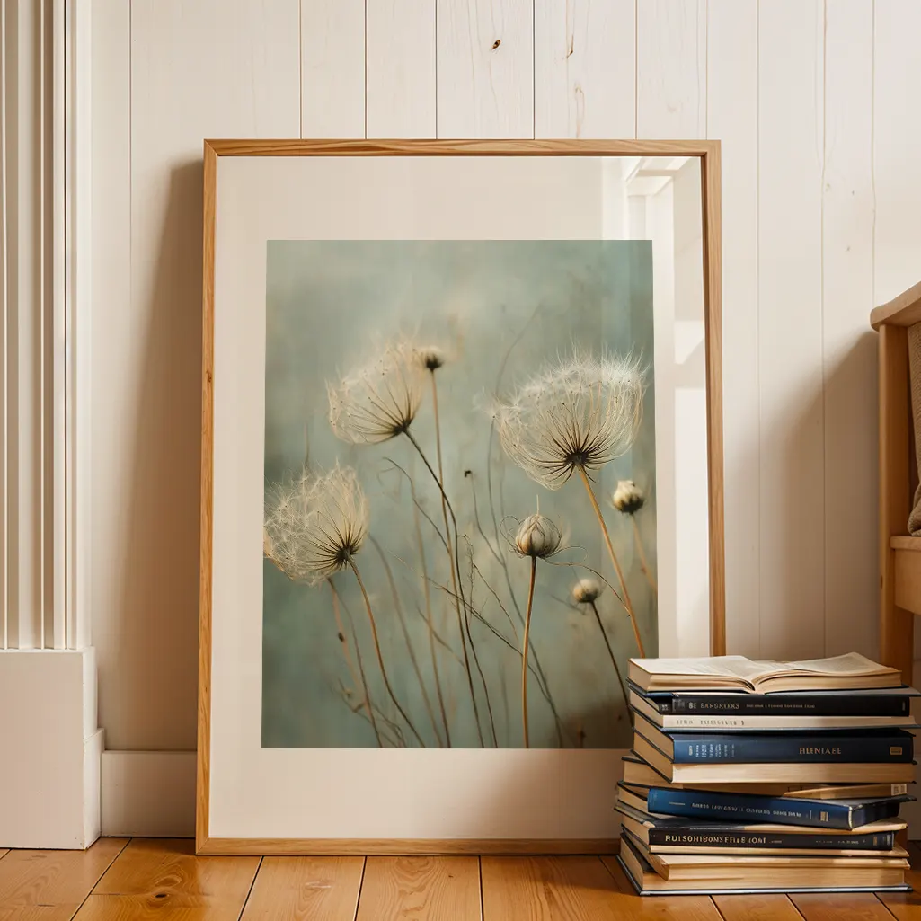 Framed botanical print of dandelions leaning against a white paneled wall, with a stack of books on the wooden floor.